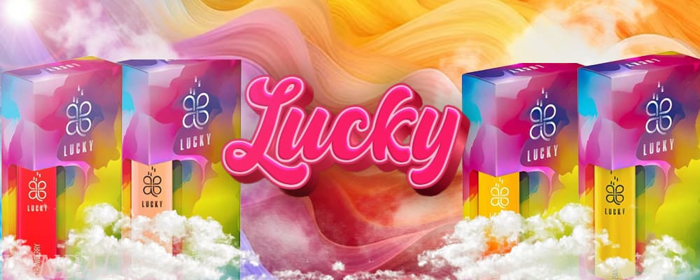 Яскравий рекламний банер з упаковками рідин LUCKY на фоні райдужного градієнта та хмар пари. У центрі — об’ємний напис 'Lucky' у рожевому стилі